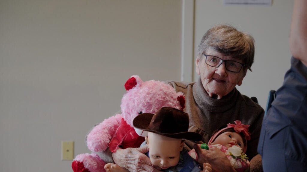 A woman holds up her stuffed animals at a long term care facility