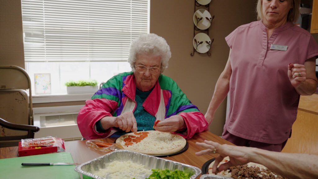 A woman makes a pizza, an activity available for short term care and respite care patients